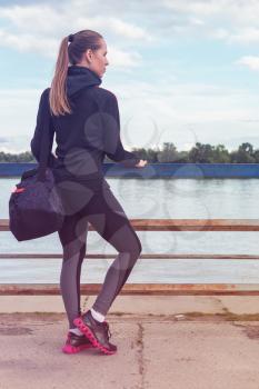 A woman in sportswear with bottle of water on embankment background