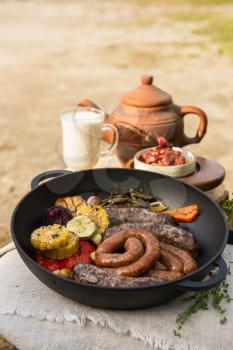 Grilled meat sausages with vegetables and spices, milk and teapot on background