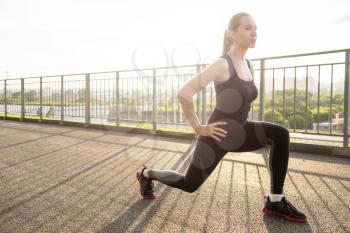 A woman in sportswear doing fitness exercises. City in sunny evening.