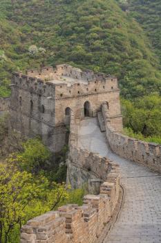 The Great Wall of China watchtower with arched windows and viewing platform against mountain hill covered forest