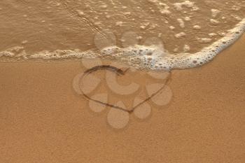 Heart drawing in the sand and wave on the morning beach