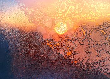 Nature background with ice pattern, bright sunlight and water drops on winter window glass