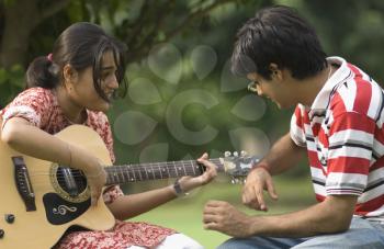 Woman playing guitar with her boyfriend in a park