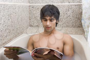 Man relaxing in the bathtub and reading a magazine