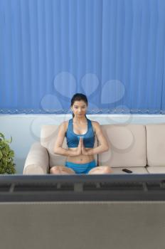 Young woman practicing yoga in front of television