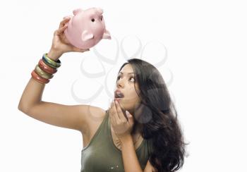 Young woman looking at a piggy bank in shock