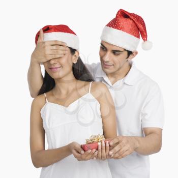 Man covering his girlfriend's eyes and giving a Christmas present