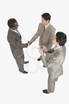 Two businessmen shaking hands with another businessman clapping