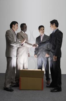 Two businessmen shaking hands over an illuminated cardboard box with their colleagues standing beside them