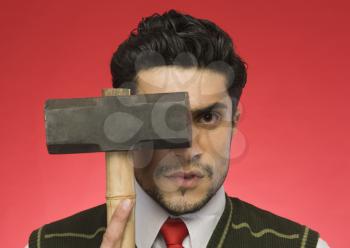 Portrait of a businessman holding a sledgehammer in front of his face