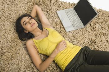 High angle view of a woman lying on a rug with a laptop