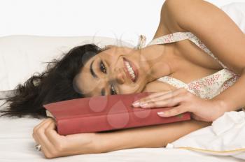 Portrait of a woman lying on the bed with a book and smiling