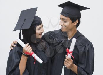 Couple in graduation gown holding diplomas and smiling
