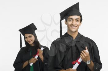 Couple in graduation gowns holding diplomas and smiling