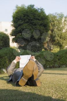 Businessman lying and reading a paper in a park