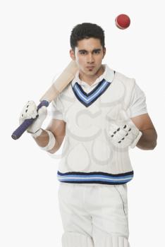 Cricket batsman holding a bat and tossing a ball