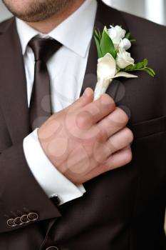 The groom holds his boutonniere hand. The groom in suit and boutonniere