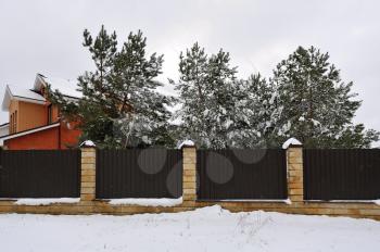 Fence near the house with pines, in winter