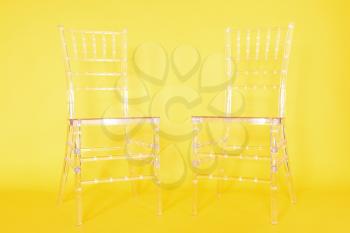 Transparent plastic chairs on a yellow background in a photo studio.