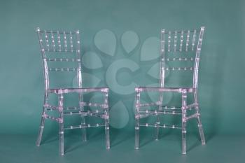 Transparent plastic chairs on a green background in a photo studio.