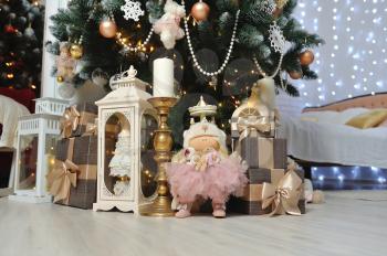New Year's decor in beige under the Christmas tree, gifts, lights, house and candles.