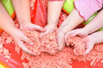 Children play with pink kinetic sand for sculpting figures. Top view