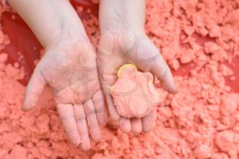 A child plays with pink kinetic sand for sculpting figures and shows his hands with a figure. Top view
