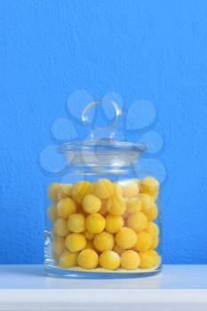 beautiful fresh yellow sugar dragees are stored in a glass transparent jar against the background of the blue wall