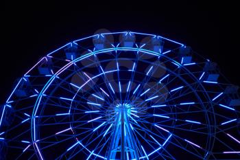 Glowing ferris wheel in an amusement park against a black night sky.