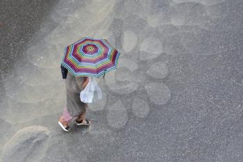 A woman with an umbrella and a grocery bag runs through a large stream of water during heavy rain.
