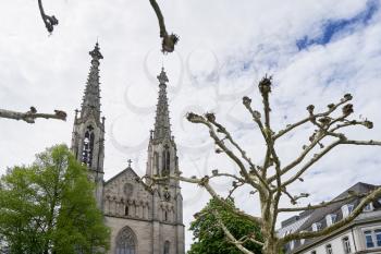 Branches of a platanus tree against the background of an evangelical church with towers in Europe. August Square, Baden Baden