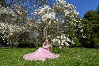 A young girl in a lush pink dress next to a large and blooming magnolia tree. Girl and tree with white magnolia flowers