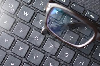 Black-rimmed eyeglasses lie on the laptop keyboard as a symbol of vision loss and fatigue.