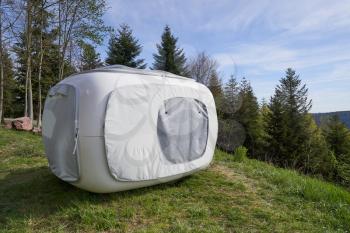 Unusual tent in the form of a cube for outdoor recreation or sleep, set on the mountainside next to the forest
