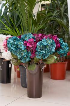 Artificial flowers are hydrangea turquoise and crimson. Artificial flowers stand on a floor in a vase.