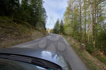 Photo from the window of a car that is driving along a road with a cliff and turns along the forest Schwarzwald, Germany. Car hood and forest road