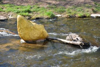 A large stone painted in gold color lies in a city river