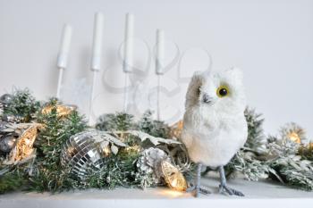 A white owl figurine stands on a shelf with candles decorated for Christmas or New Year.