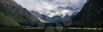 Snowy mountains and trees in a cloudy day. Khan Tengri Mountain In Xinjiang, China.