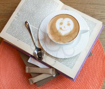 Tasty coffee cappuccino with smiling face, on a book, top view