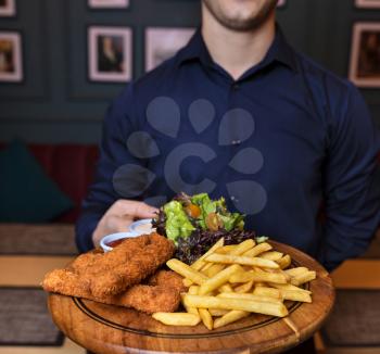 Waiter holding fried chicken and french fries on the wooden plate