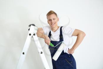 Young painter with roller standing on ladder against white background�