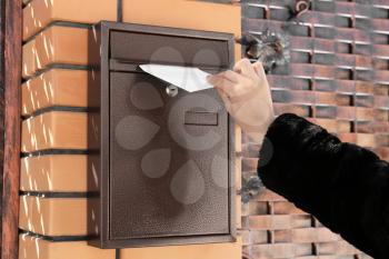Woman putting letter in mailbox outdoors�