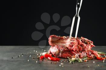 Composition with meat fork and raw steaks on table against black background�