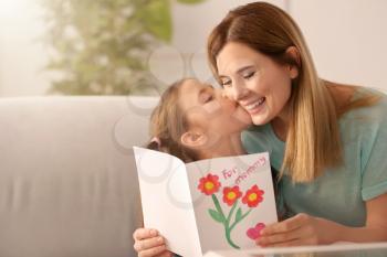 Mother receiving greeting card from her cute little daughter at home�