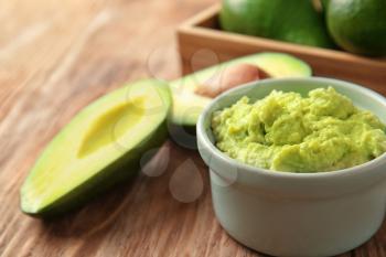 Bowl with tasty guacamole and ripe avocados on wooden table�