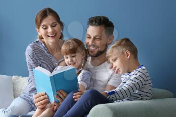 Parents and their children reading book together at home�