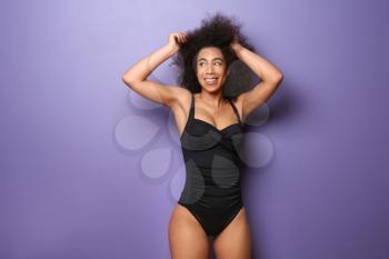 Beautiful African-American woman in swimming suit on color background�