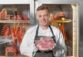 Young man holding piece of raw meat in butcher shop�