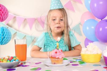 Little girl blowing out candle on birthday cupcake at home�